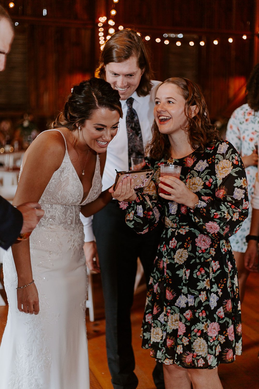 Bride laughs looking at guest's phone at wedding reception