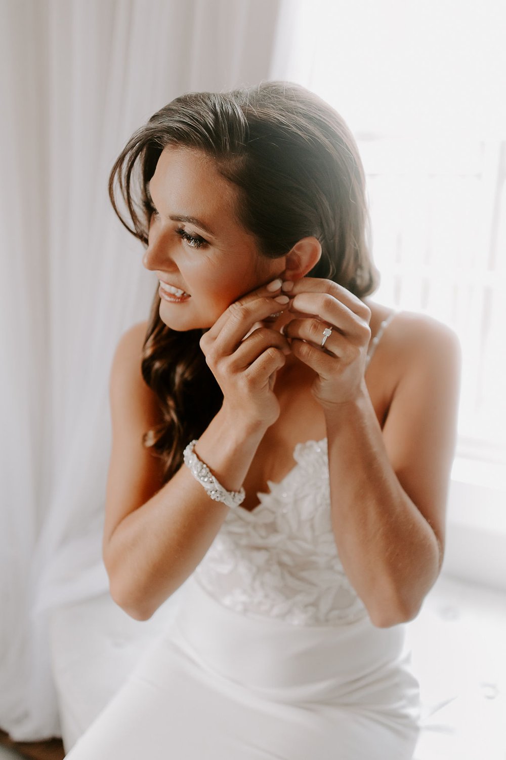 Bride puts on earrings as she gets ready for wedding day