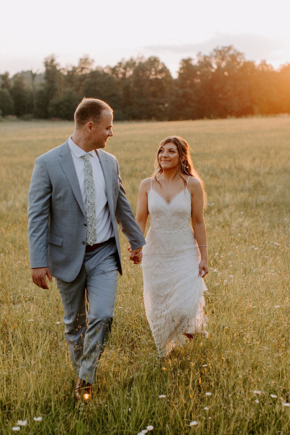 Couple walks holding hands in wedding sunset field photos