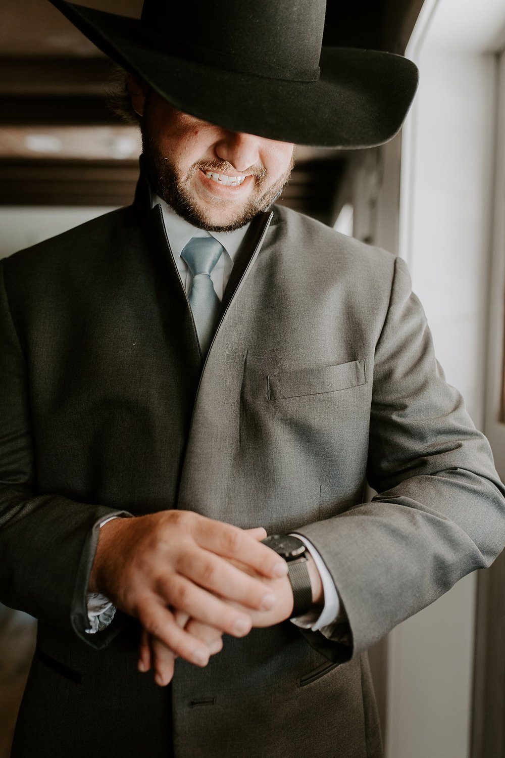 Groom wearing cowboy hat puts on watch on wedding day