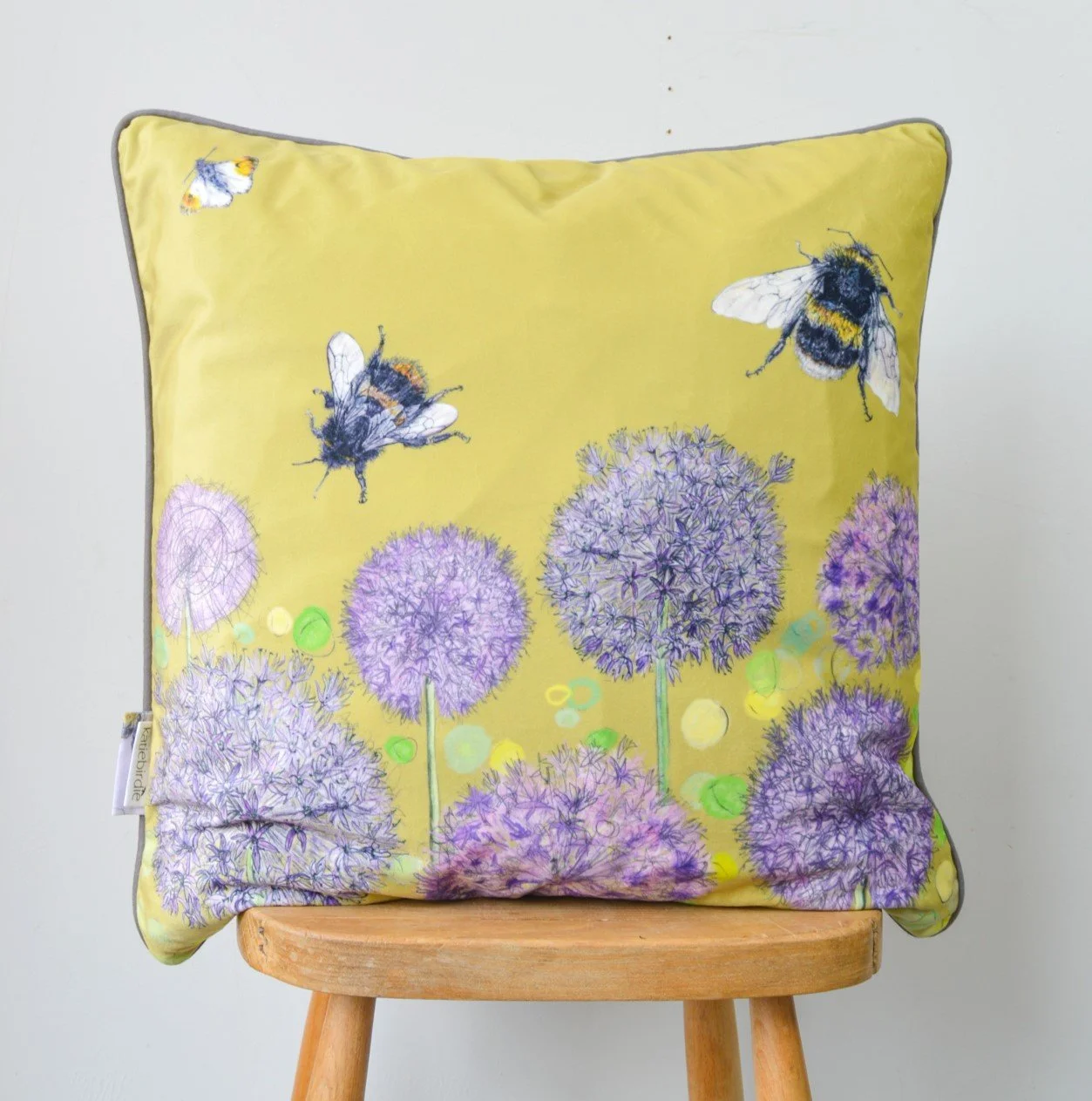 Decorative pillow with a yellow background featuring purple allium flowers, bees, and small green and yellow circles.