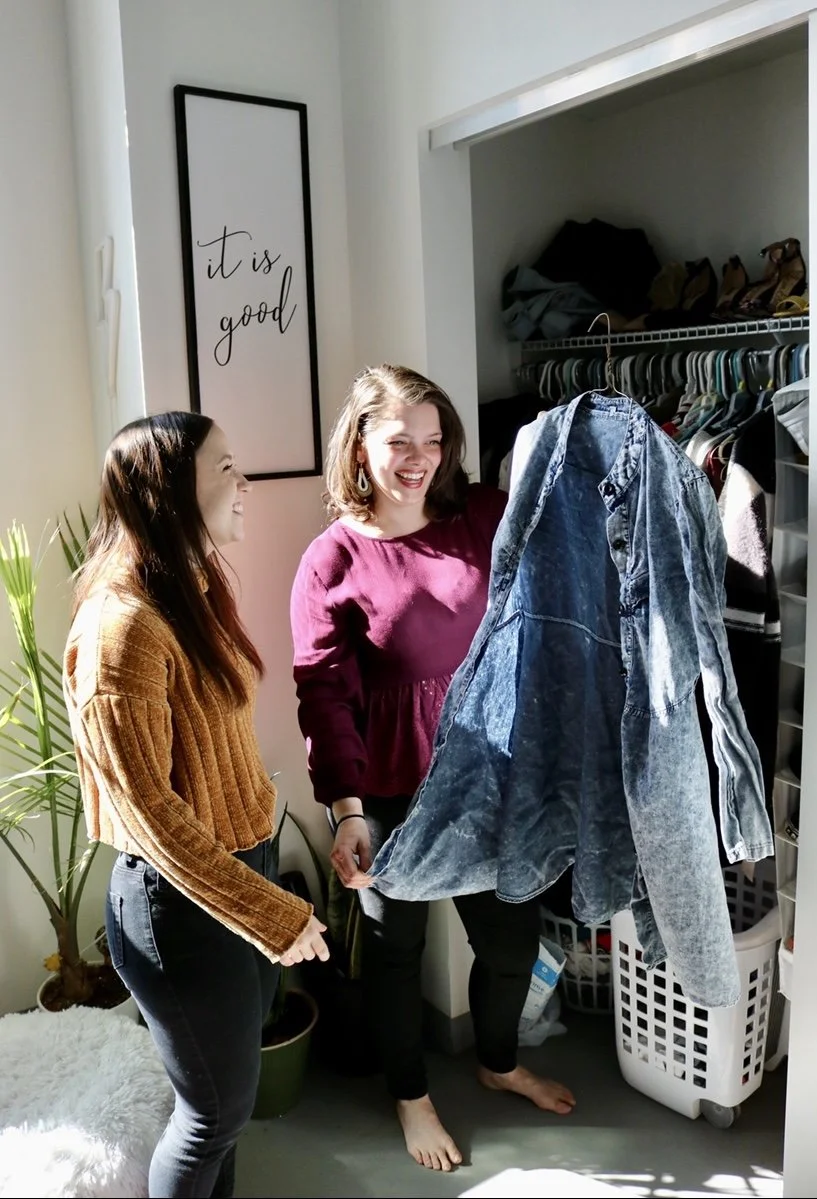 Personal Stylist, Taylor, holds a garment from her client's closet. She and her client admire the item and laugh while discussing how to wear it.
