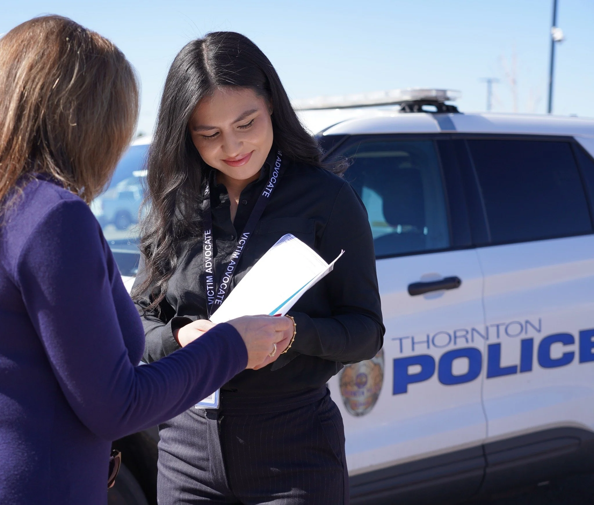 victim advocate providing pamphlet to victim with police car in the background
