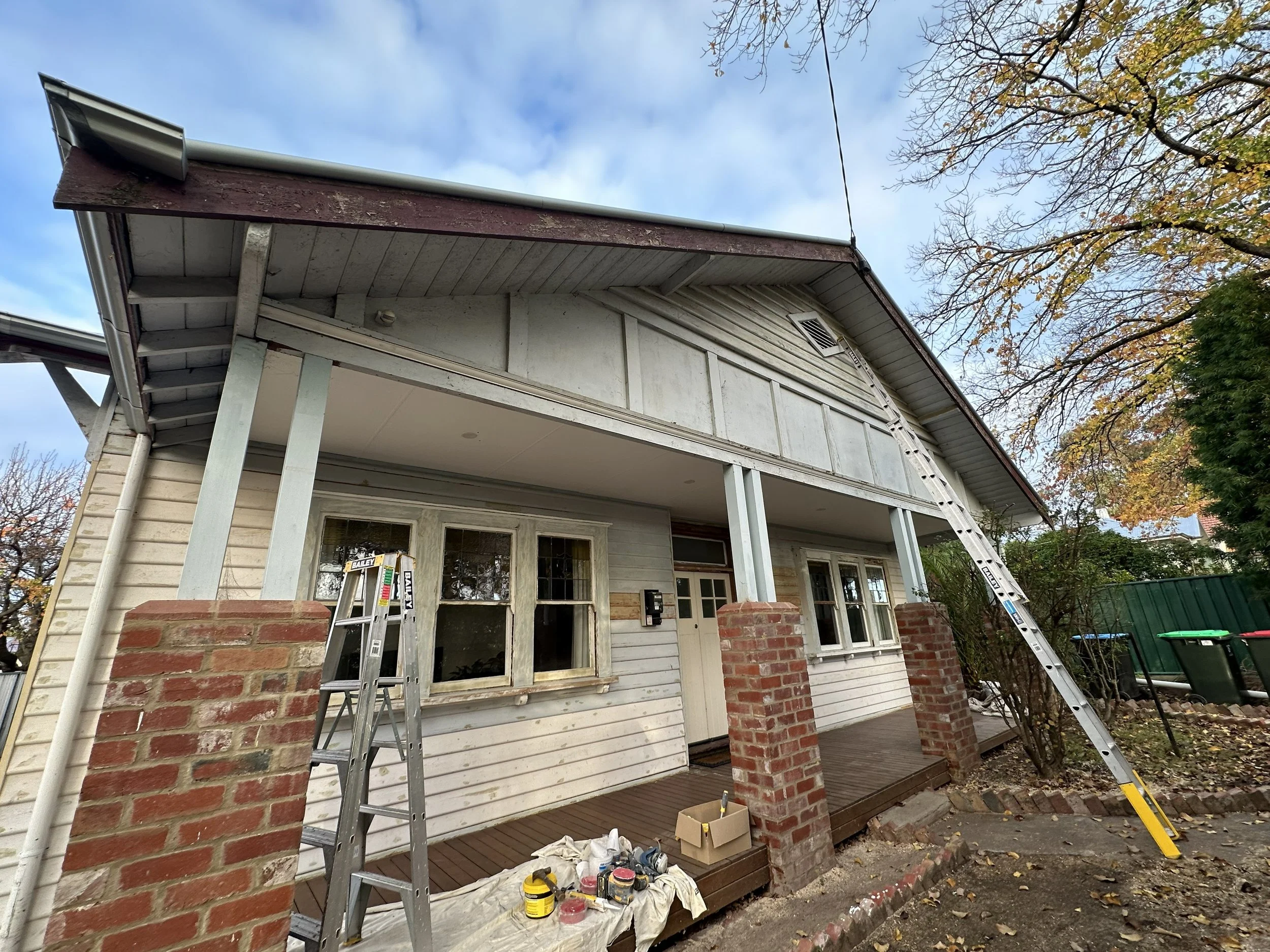 Before photo showing weathered weatherboard exterior with peeling paint and damaged boards.