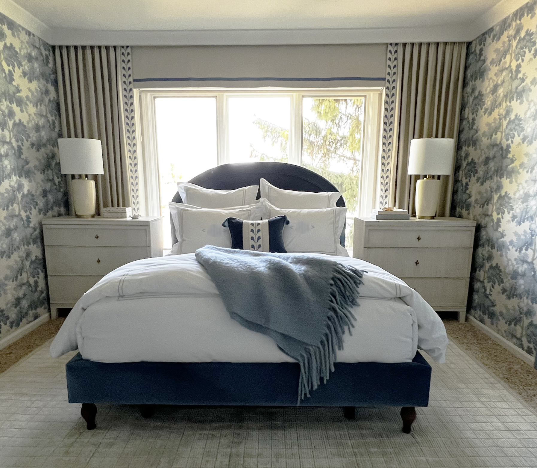Blue and white bedroom with warm neutrals wallpapered in Sandberg Raphael wallpaper with a custom upholstered bed frame, custom frame for the TV, and custom built in vanity area with lit mirror