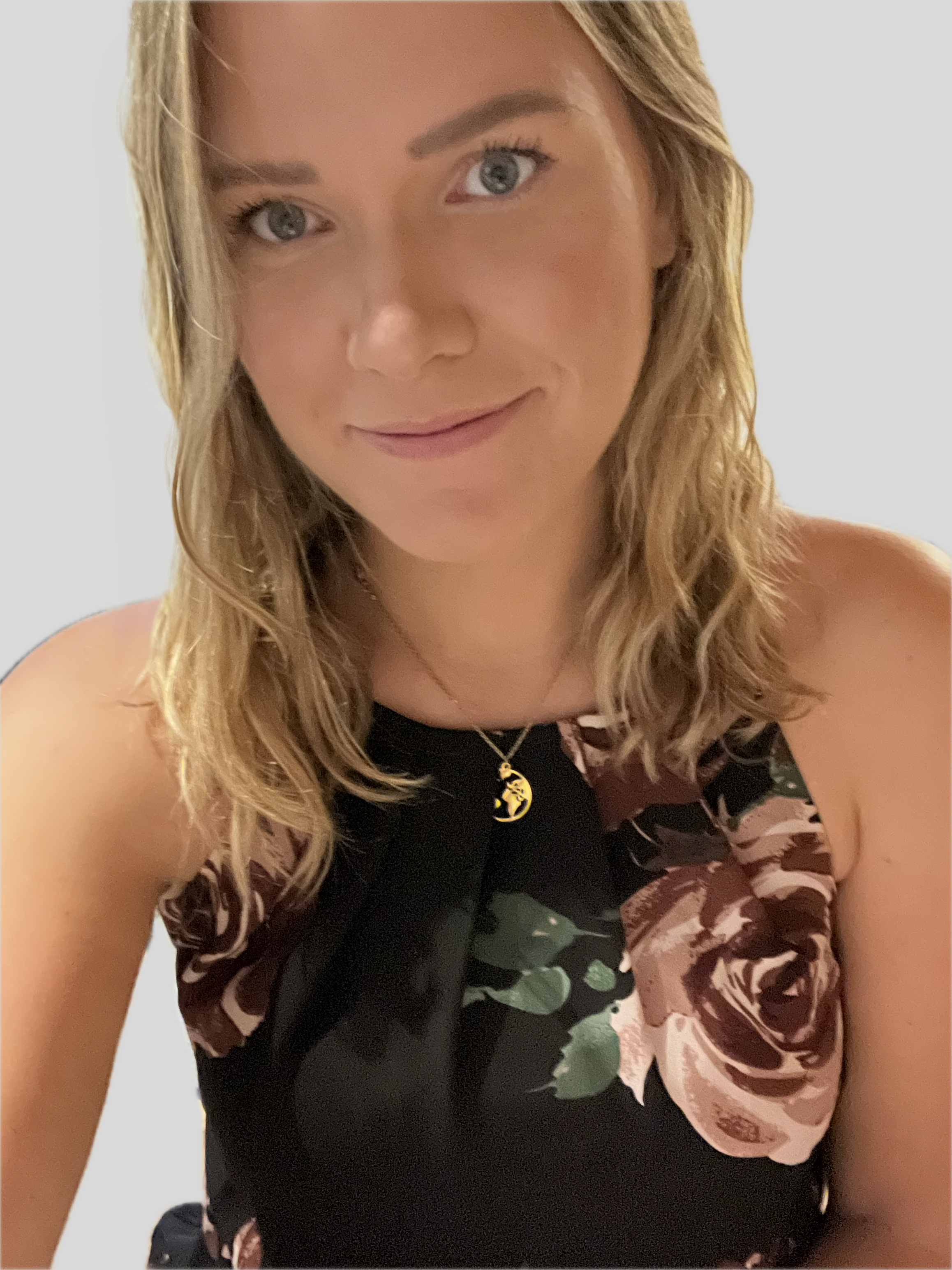 A young woman with wavy blonde hair and blue eyes, wearing a black floral top and a gold necklace with a moon and star pendant, smiling at the camera.