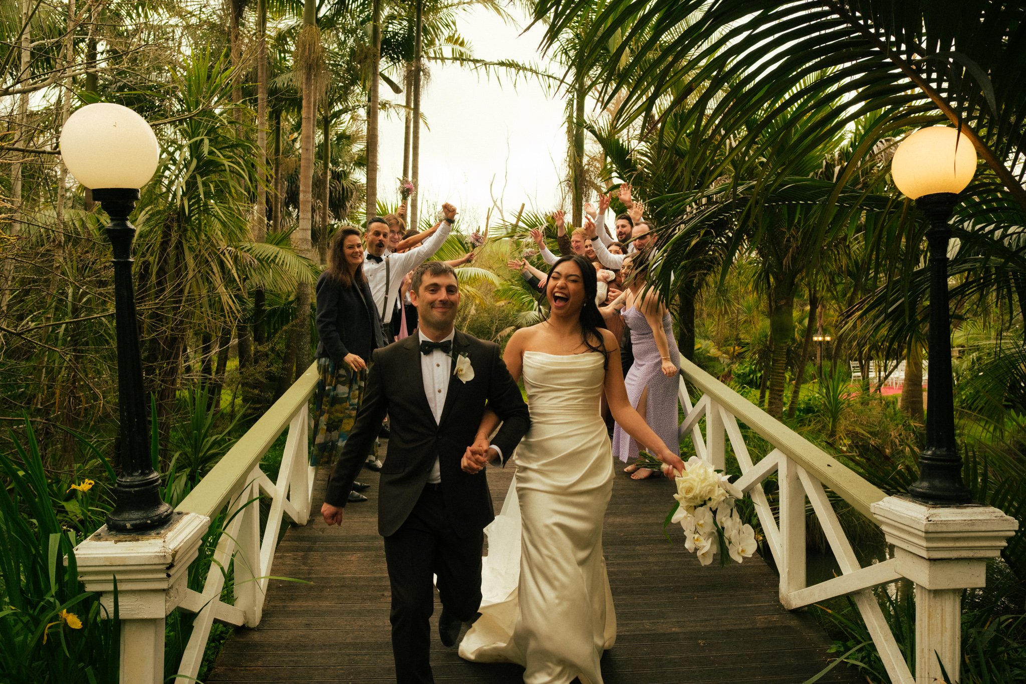 Charisse Uy and Chris Groen walk through a makeshift arch comprised of their bridal party and family members. Taken at Settlers Country Manor, Auckland, New Zealand by Jille Cristobal of Reina Jille Photography, an Auckland wedding photographer.