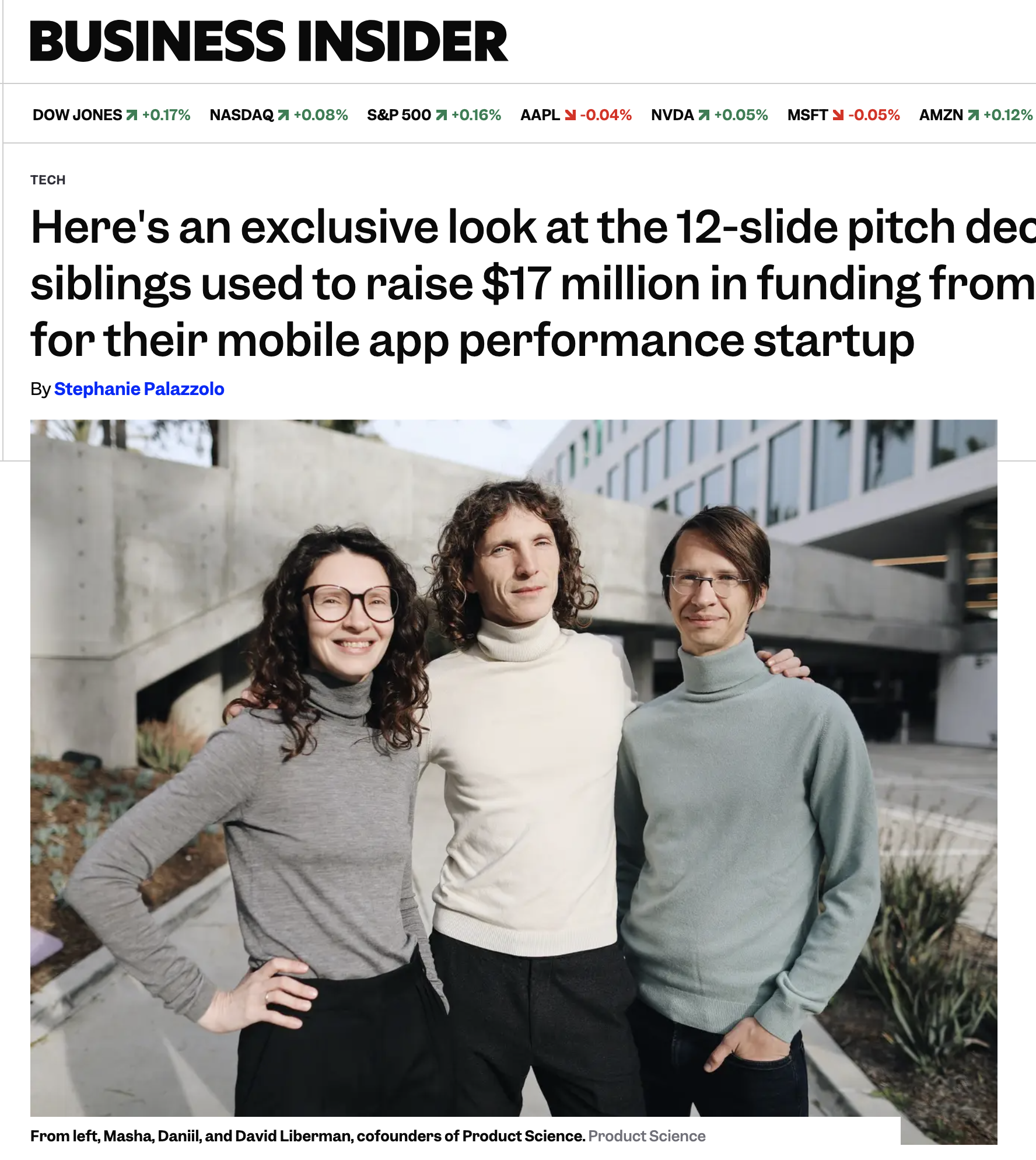 Three young adults, two women and one man, standing outdoors in front of a modern building, smiling at the camera. The woman on the left has curly dark hair, glasses, and is wearing a gray turtleneck sweater. The woman in the middle has curly hair an