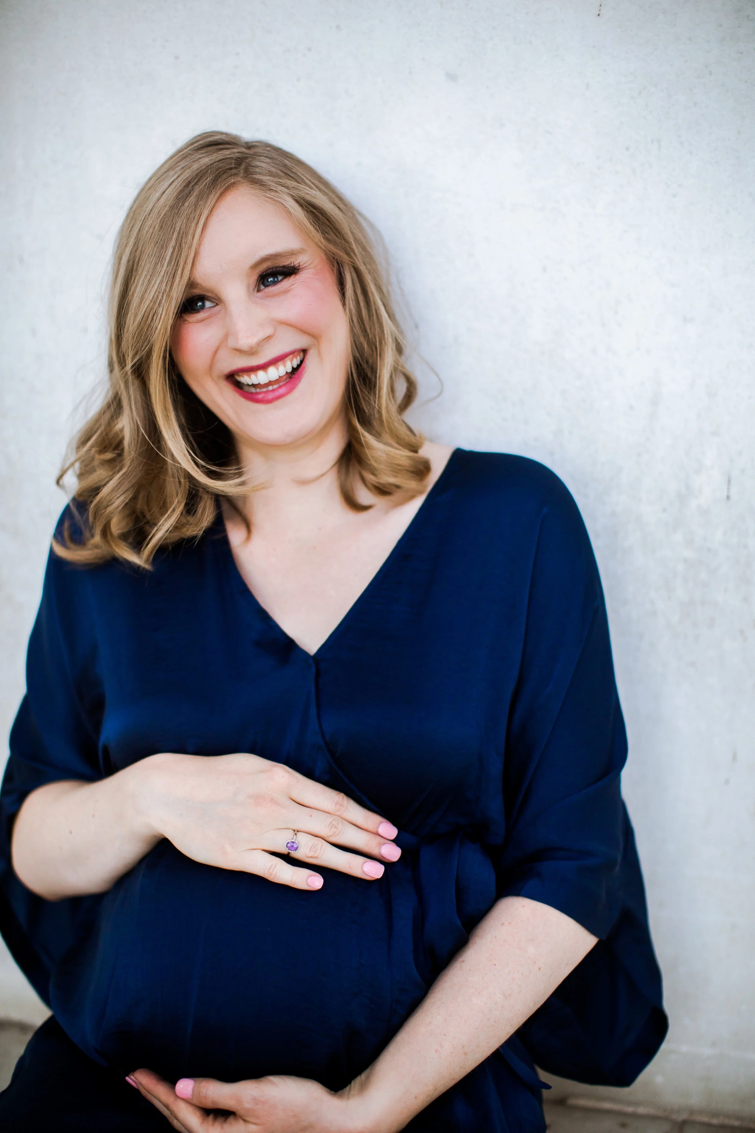 blonde woman smiling while wearing a blue v neck dress