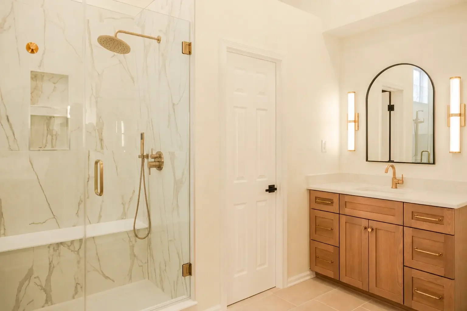 Custom bathroom remodel in Dublin, Ohio featuring a larger walk-in marble shower with bench seating, frameless glass enclosure, custom 48-inch oak vanity, quartz countertops, and brushed brass fixtures by Elevate Remodeling.