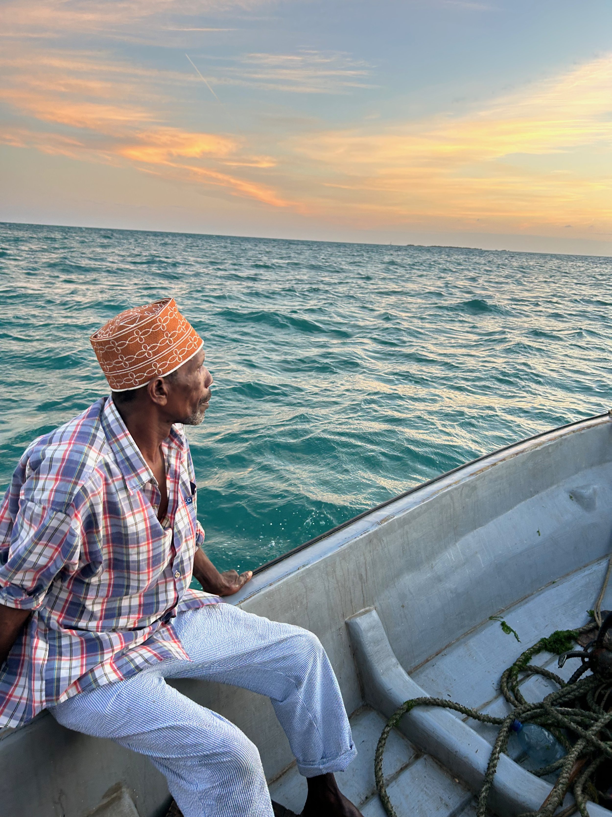 Ein älterer Mann mit indischer Kleidung sitzt in einem Boot auf dem Meer während des Sonnenuntergangs.