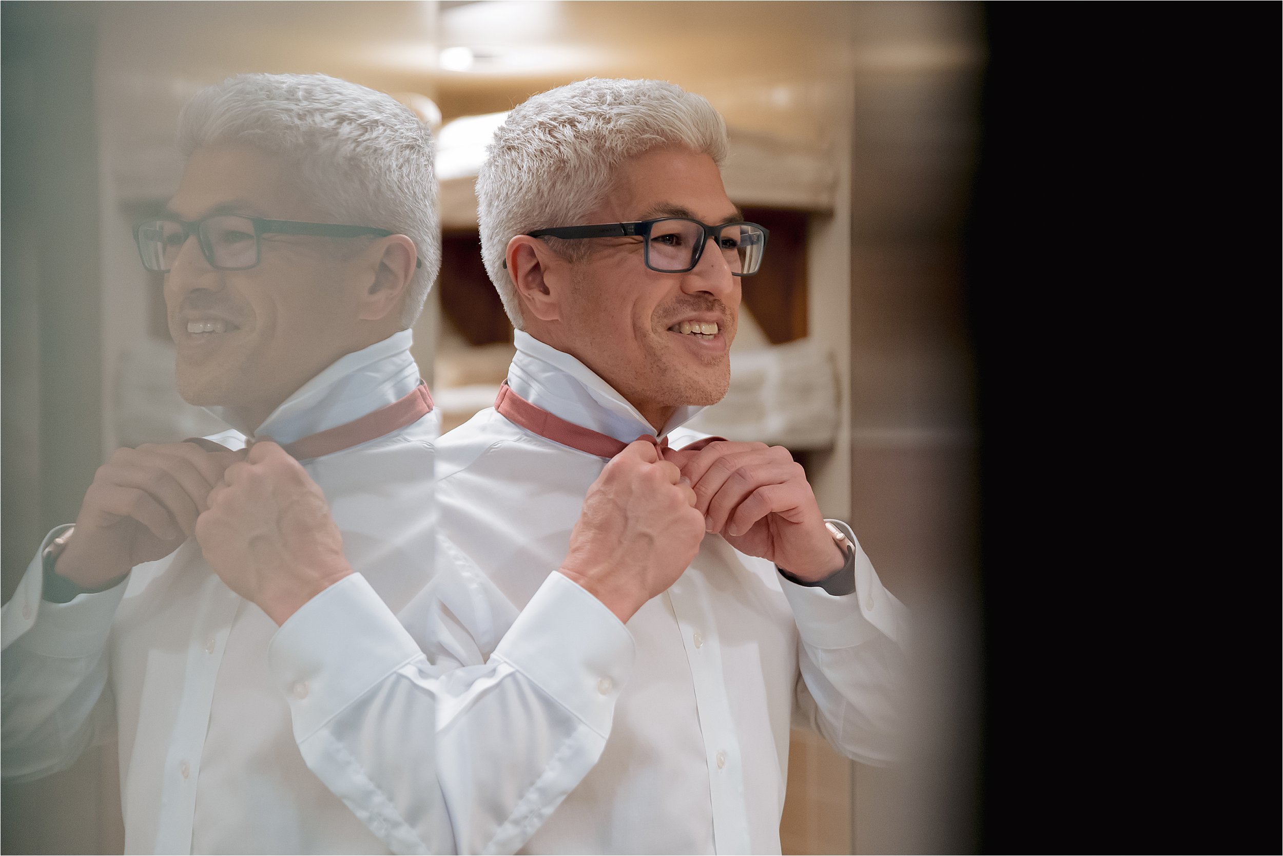 Groom adjusting collar in mirror before wedding ceremony in Milwaukee