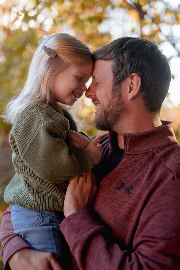 Milwaukee family photographer capturing a candid father and daughter portrait during a warm autumn session snuggling forehead to forehead