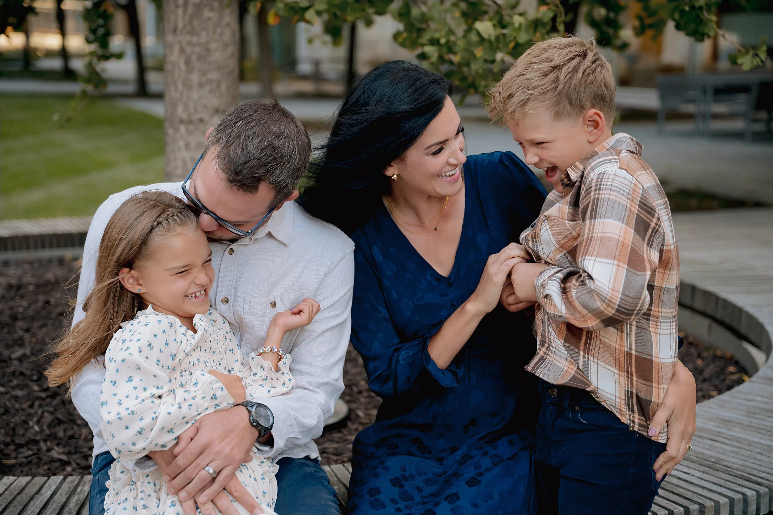 Family laughing together during a candid Milwaukee mini session in a park setting with trees and open space