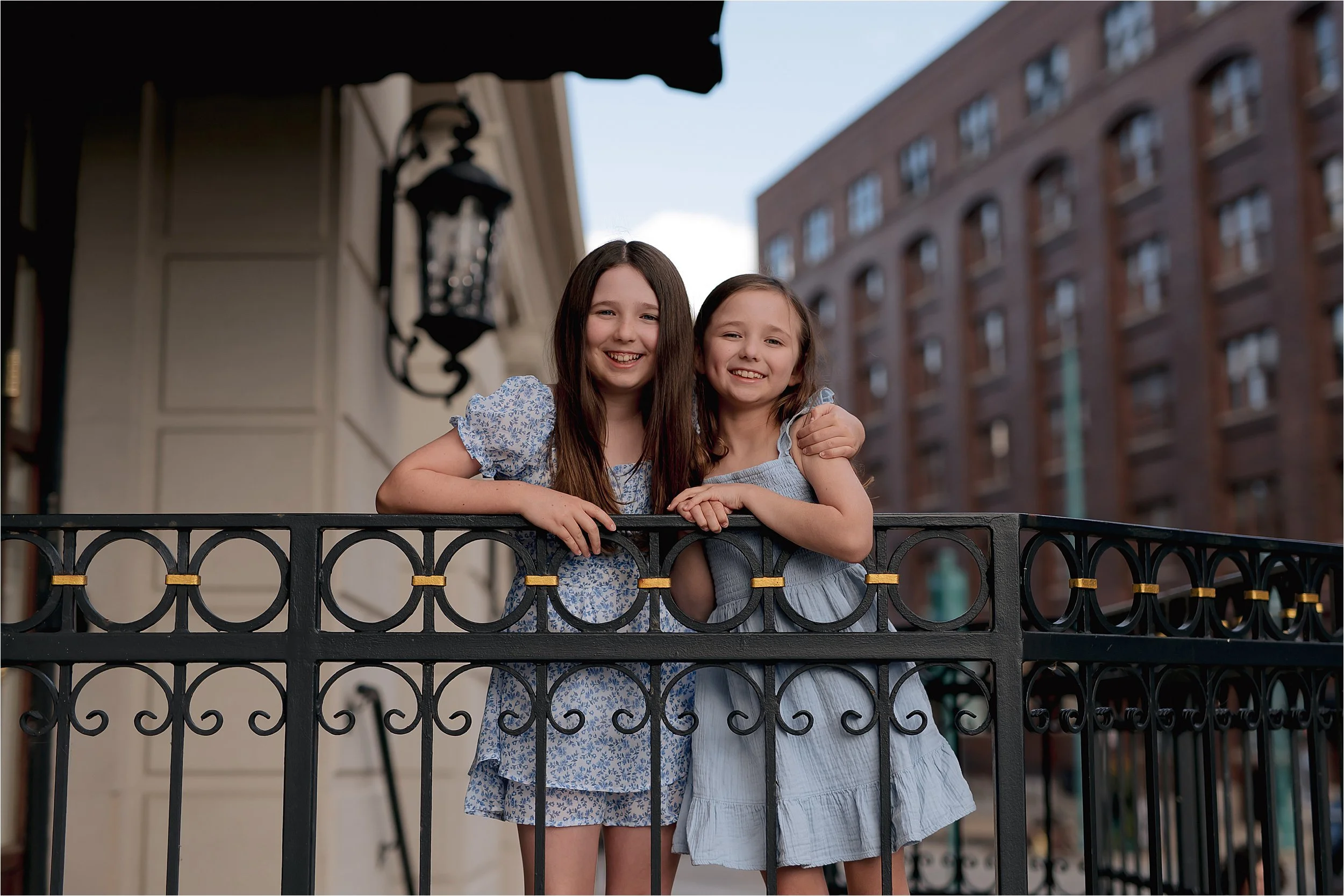 Sisters smiling on a balcony in Milwaukee’s Third Ward with historic brick buildings in the background