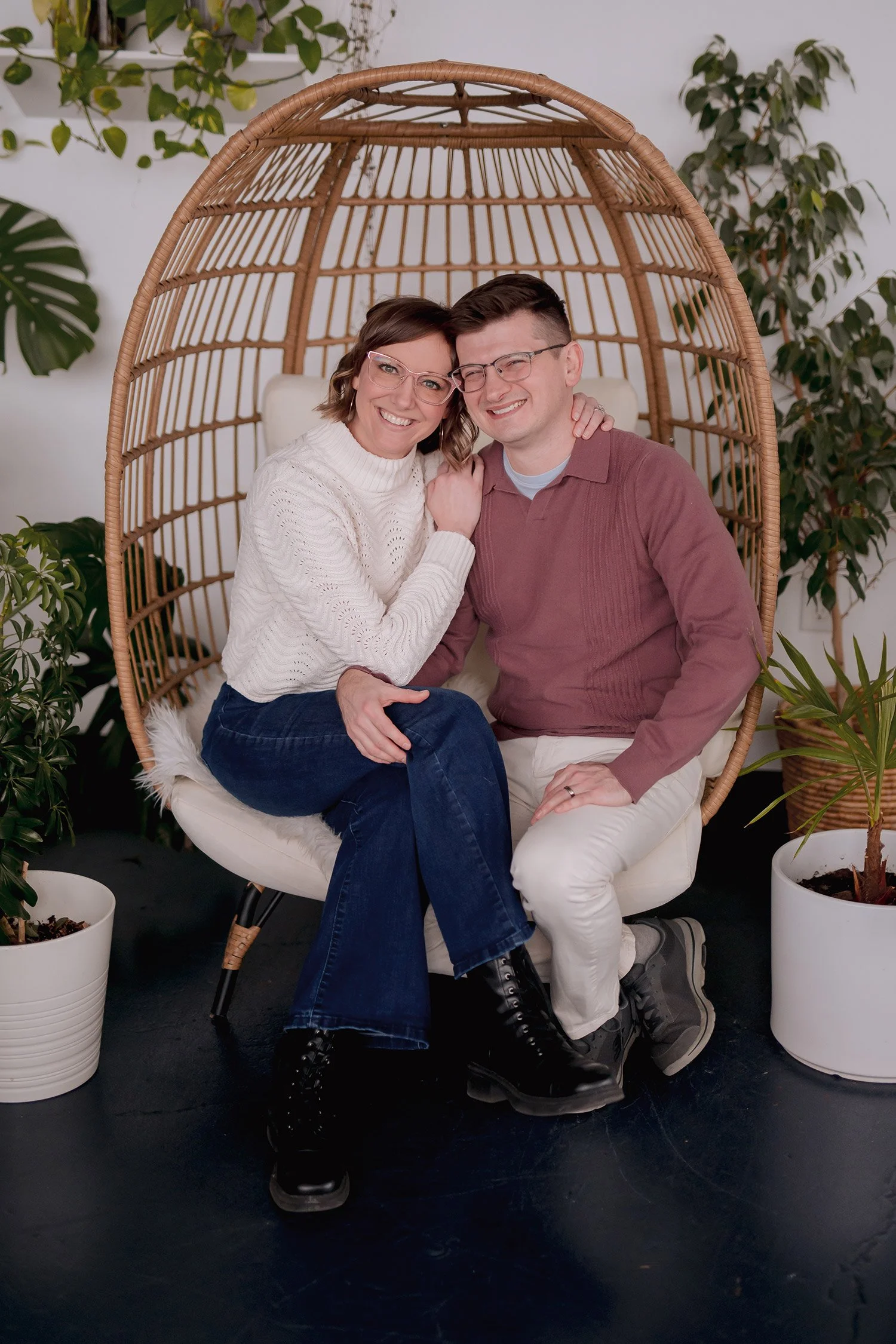 Reminisce photographers Miranda and Adam smiling at camera and sitting in rattan chair with plants
