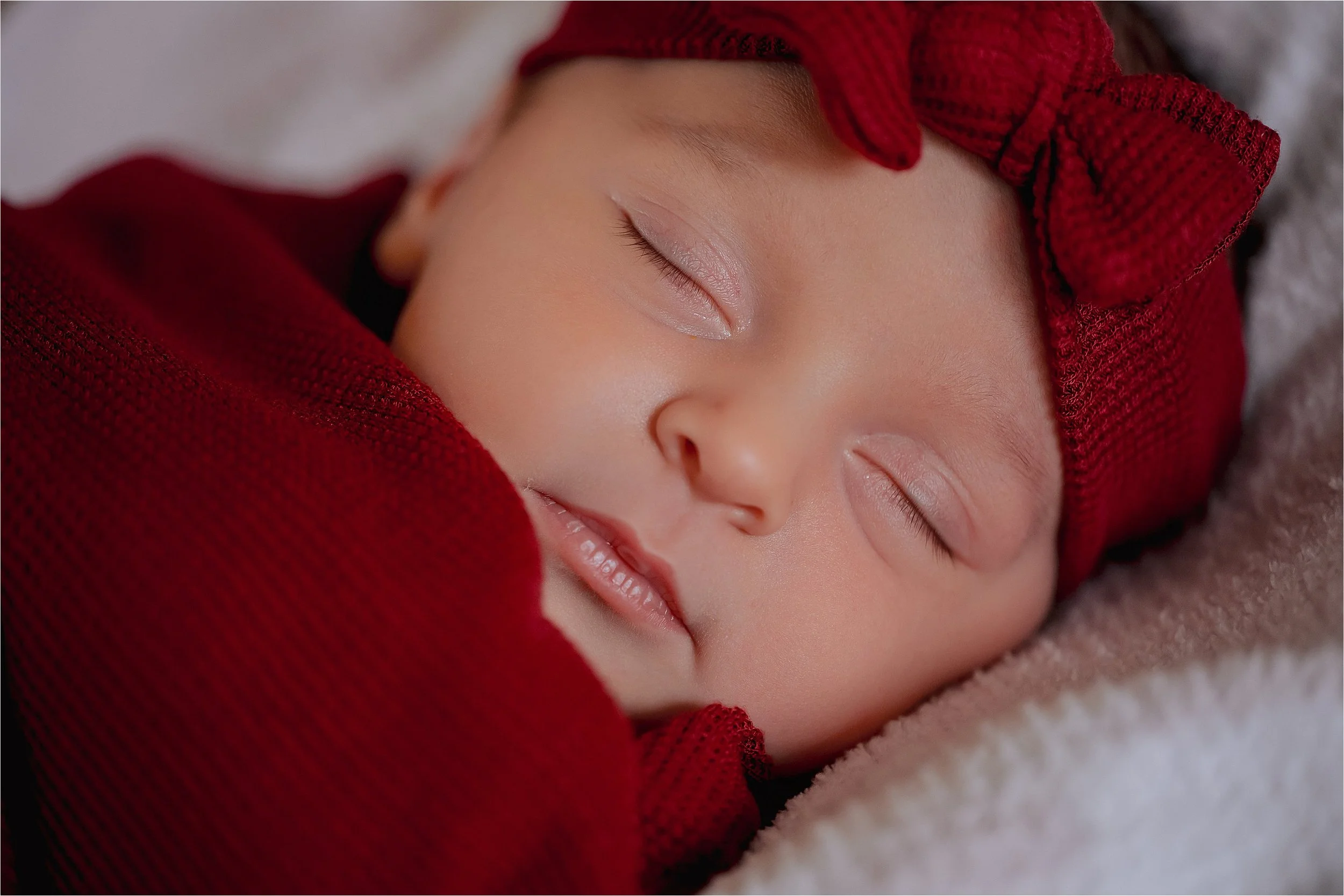 Newborn baby wrapped in red blanket sleeping peacefully during a studio newborn photography session in Milwaukee