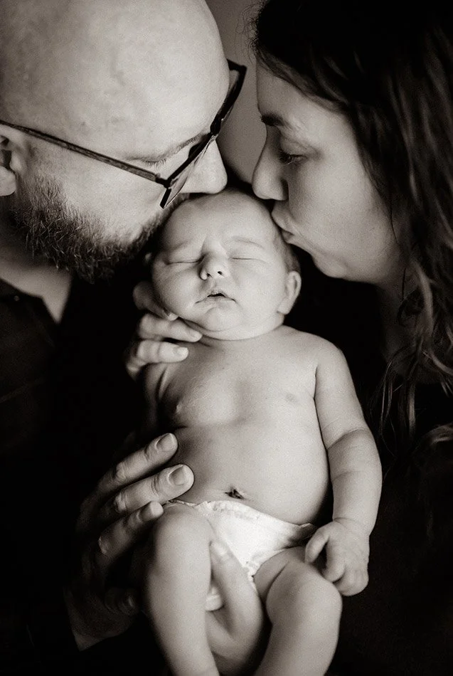 Parents kissing their newborn baby during a black and white lifestyle newborn photography session in Milwaukee