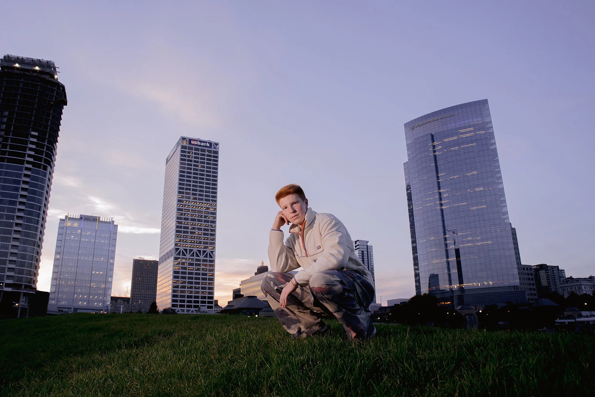 senior-boy-crouching-downtown-buildings-in-background-hand-to-side-of-head.JPG