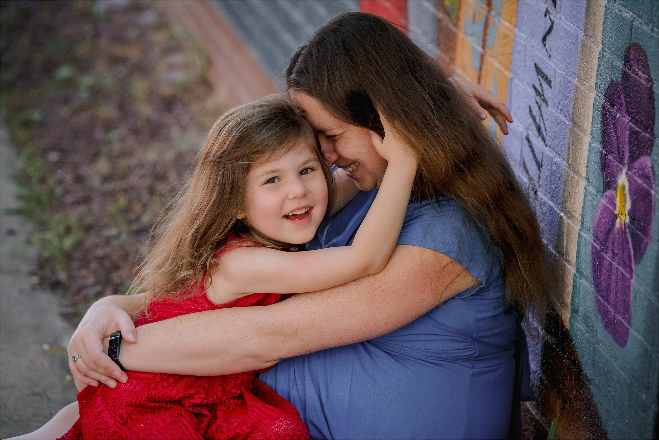 Mother hugging young daughter during maternity session by colorful mural in Milwaukee