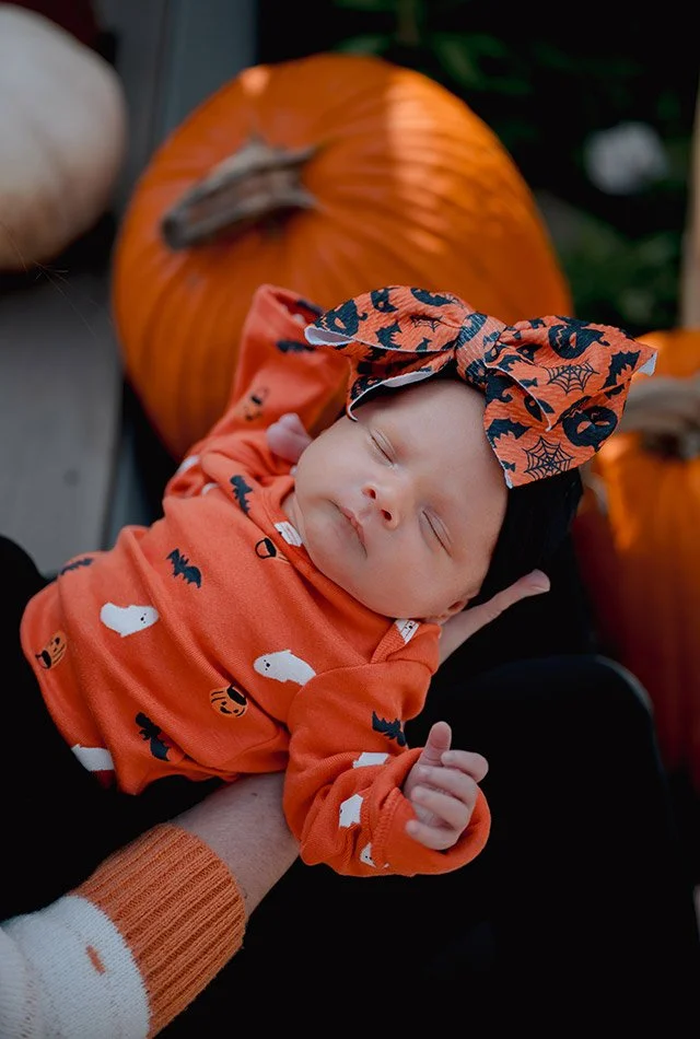 Newborn baby dressed in a festive fall Halloween outfit during an outdoor Milwaukee newborn photography session with pumpkins