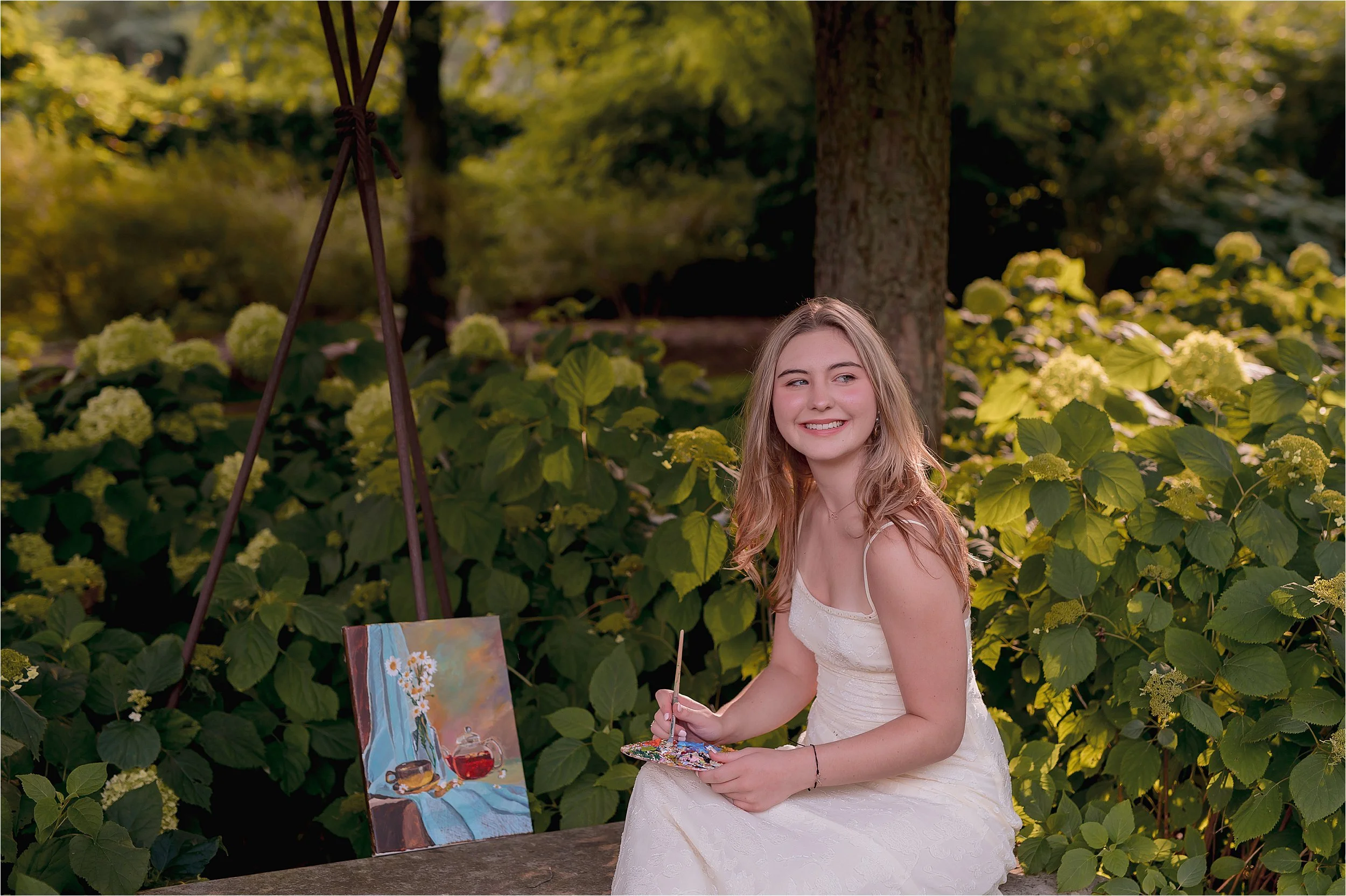 Artistic senior portrait of a student painting in a garden during a Milwaukee senior photo session at villa terrace