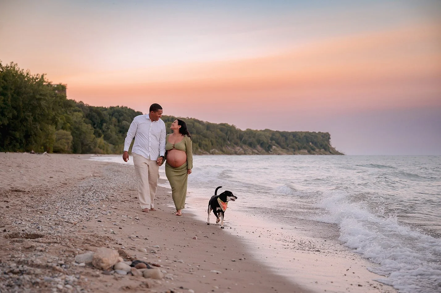 Expecting couple walking along the beach at sunset with their dog during a Milwaukee maternity photography session at Grant Park's Seven Bridges