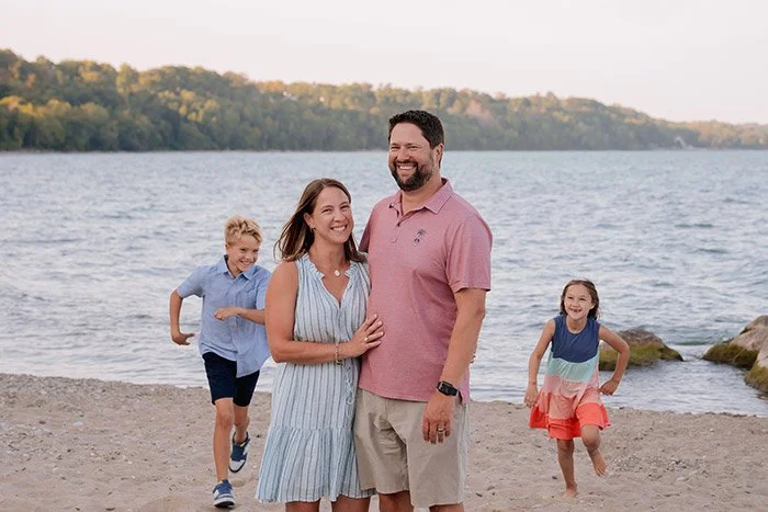 Milwaukee family photographer capturing relaxed beach portraits along Lake Michigan at sunset with kids running and playing and parents snuggling at Klode Park