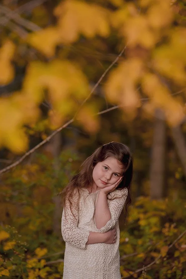 Milwaukee family photographer capturing a fall portrait of a girl surrounded by autumn leaves at Grant Park's Seven Bridges