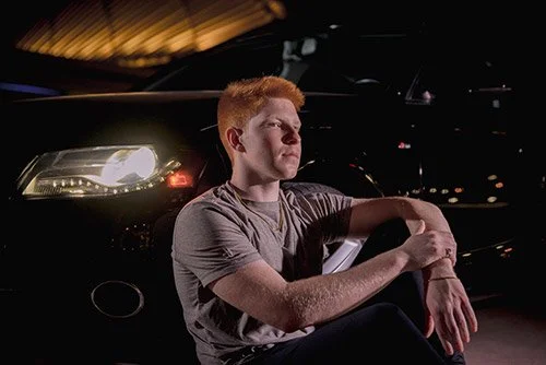 Cinematic senior portrait with dramatic nighttime lighting and creative composition in an urban setting with car headlights and the Milwaukee Art Museum