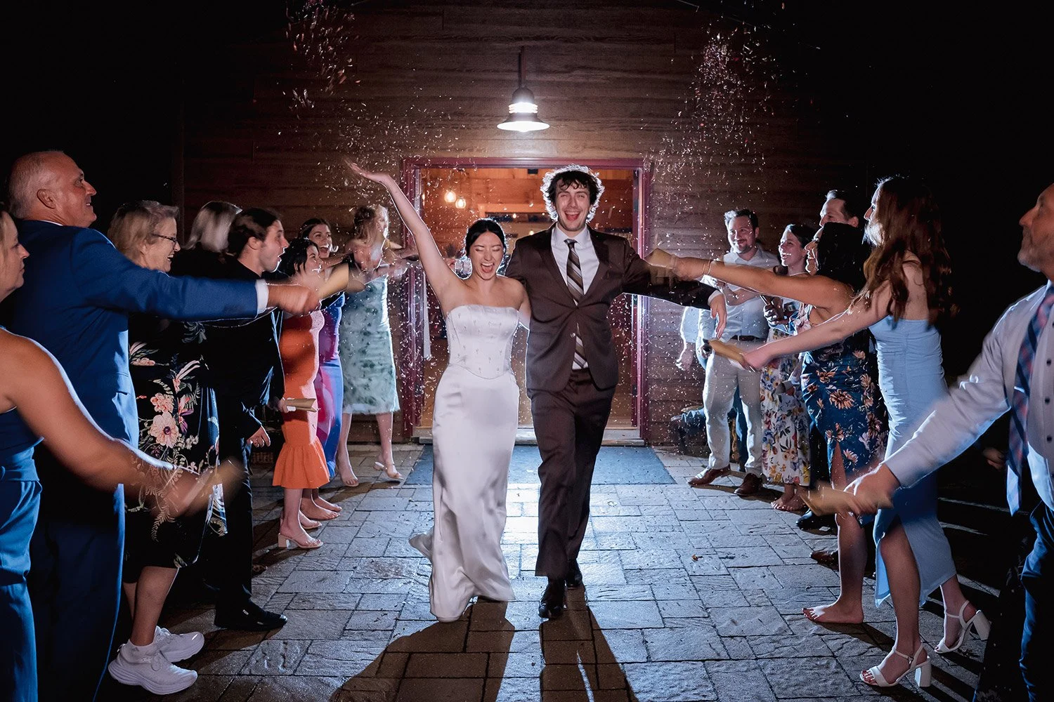 Bride and groom running through a petal exit surrounded by guests at a wedding reception in Wisconsin, captured by a Milwaukee wedding photographer at night with backlighting