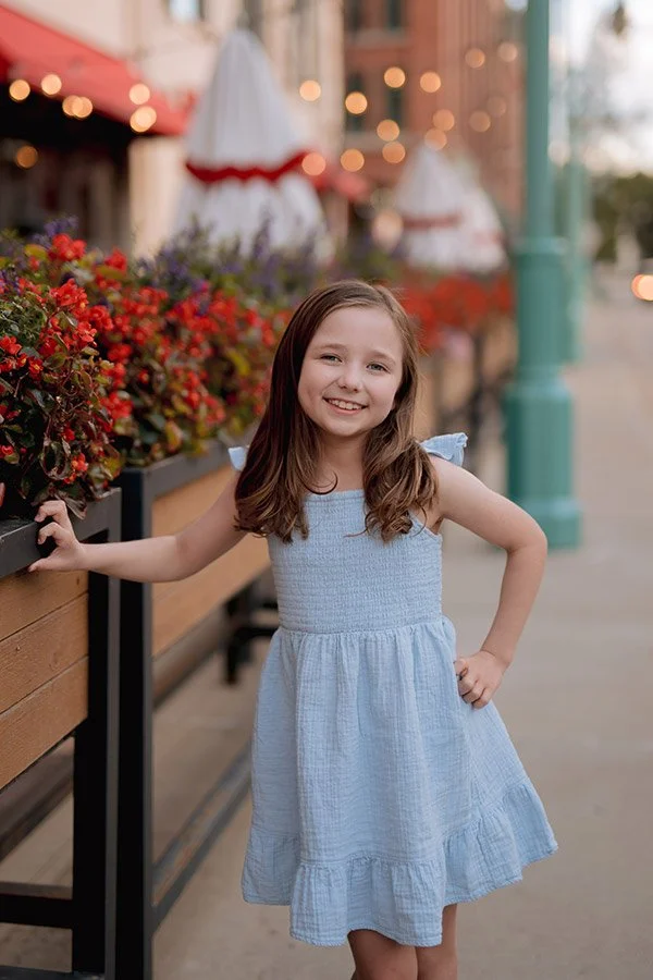 Milwaukee family photographer capturing a child portrait in downtown Milwaukee near colorful flowers and string lights in the Third Ward