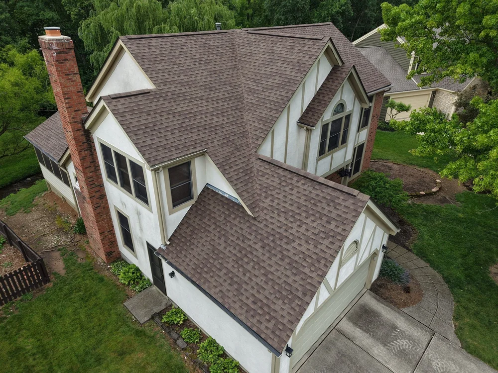 Aerial view of a new brown shingle roof on a white Tudor-style home with a brick chimney in Hilliard, Ohio