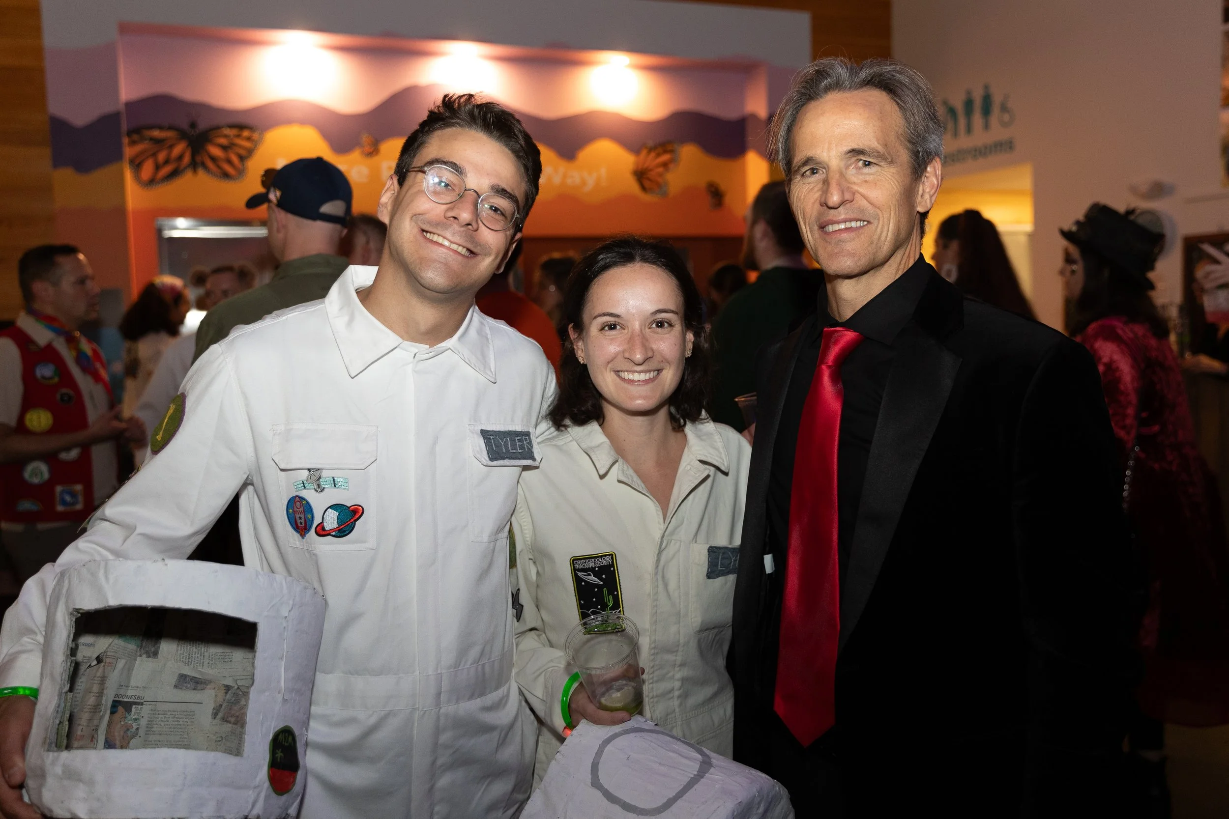 Three people are posing for the After Dark Halloween event. Two of them are dressed in astronaut costumes.