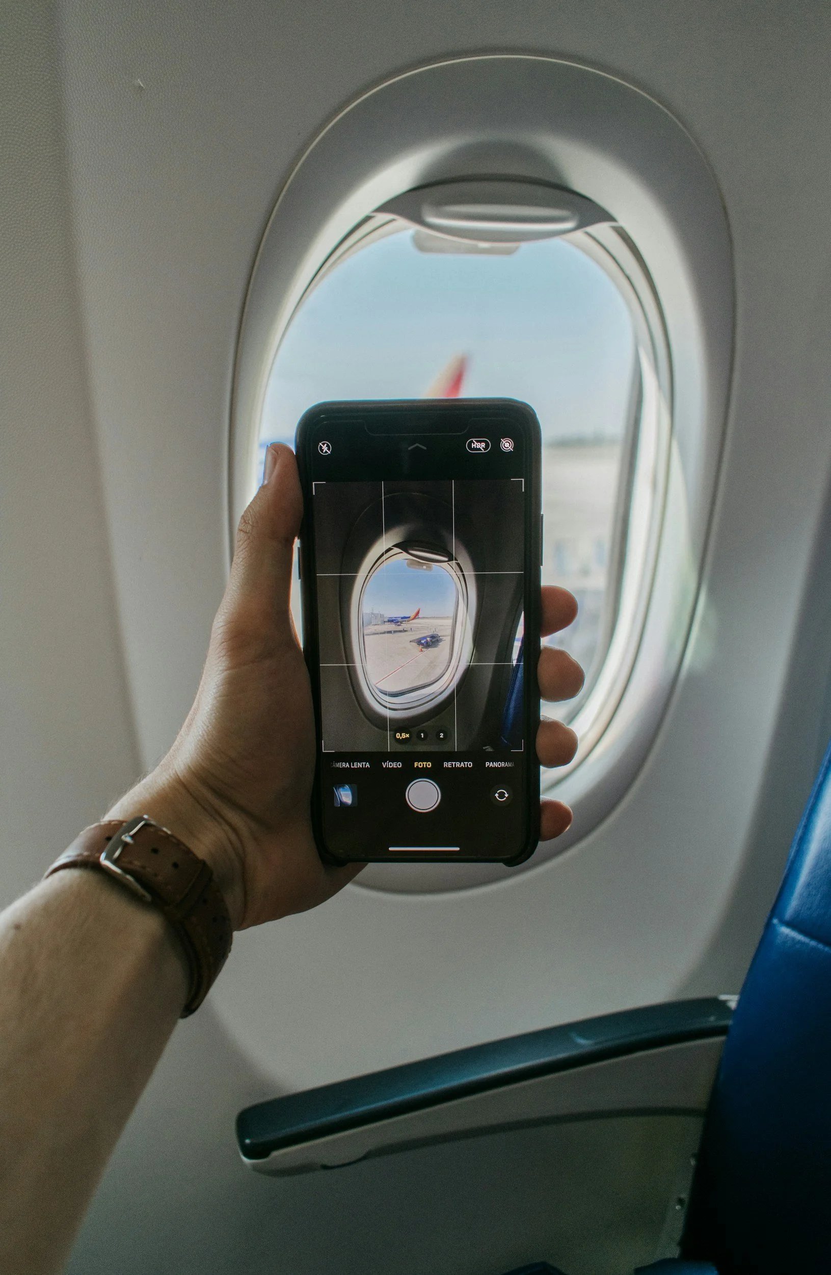 Person taking a photo of an airplane window with their phone on an airplane.
