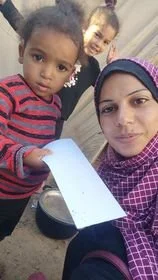 A woman wearing a pink patterned headscarf taking a selfie with two young children. One child is holding a white piece of paper.