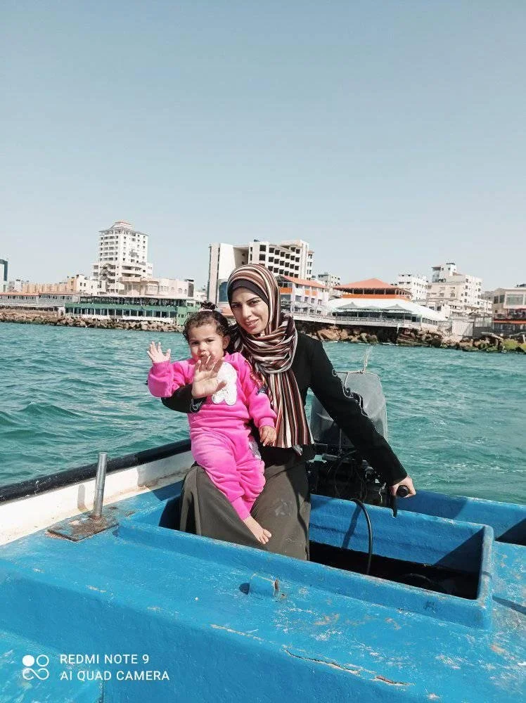 A woman and a child on a boat in a body of water with buildings in the background.