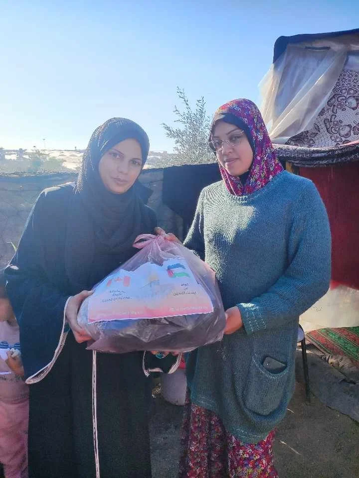 Two women holding a plastic bag containing donated goods outdoors.