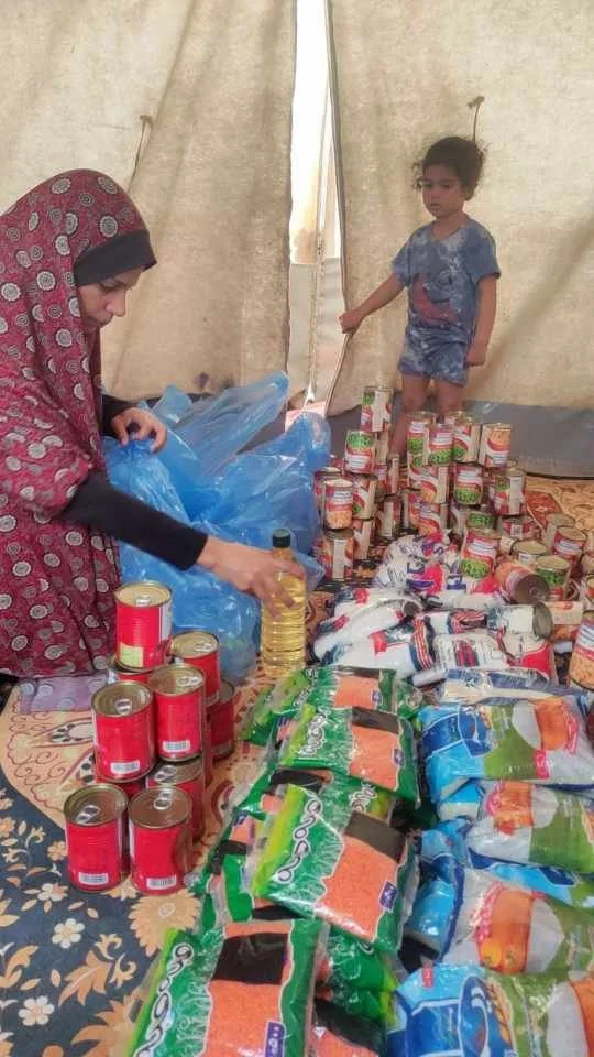 Woman and child organizing food supplies in a tent, with canned goods and packaged foods on a table.