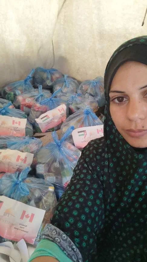 A woman wearing a headscarf in front of bags of supplies with Canadian and United Arab Emirates flags.