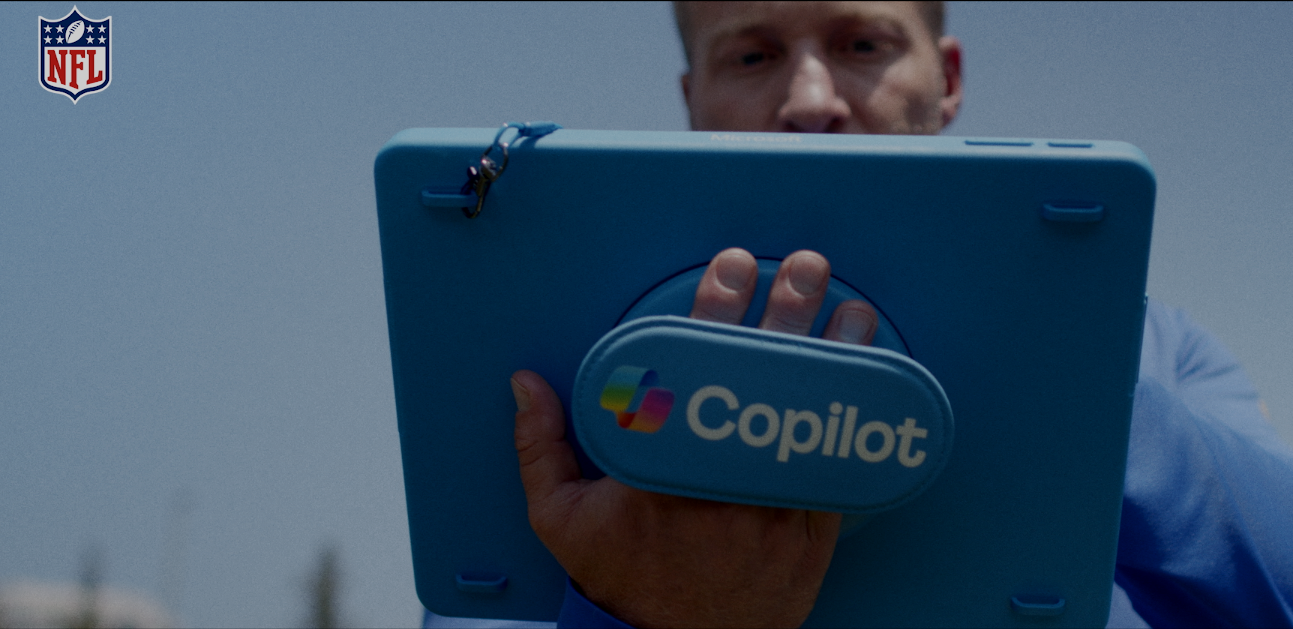 A man holding a blue tablet with a blue case that has a small attached pouch labeled "Copilot" in front of him. The background shows a blue sky, and there is an NFL logo in the top left corner.