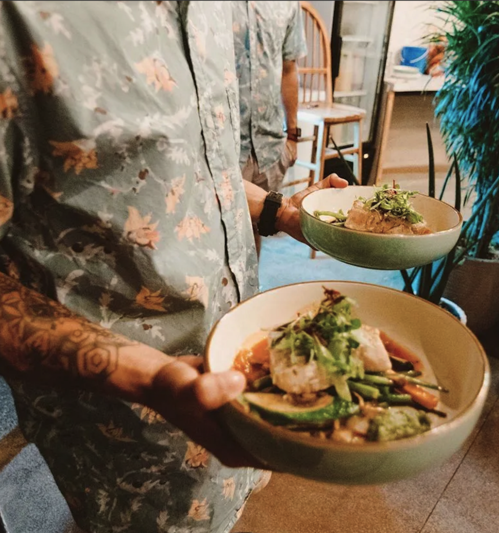 Person holding two bowls of Asian-inspired dishes, with one dish featuring fish, vegetables, and herbs.