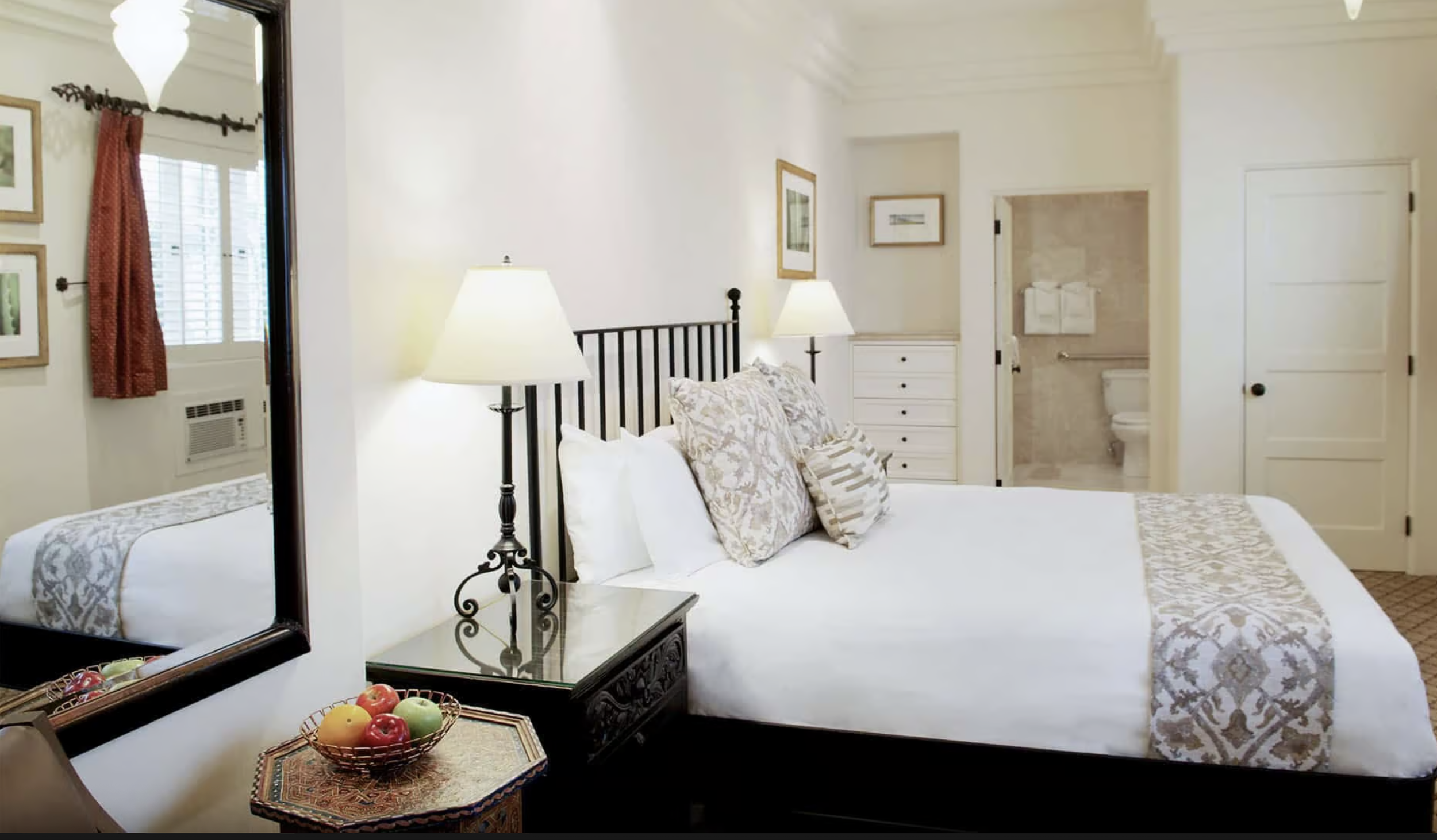 Hotel room with a four-poster bed, a fireplace, a flat-screen TV, large arched windows, and a balcony with outdoor seating.