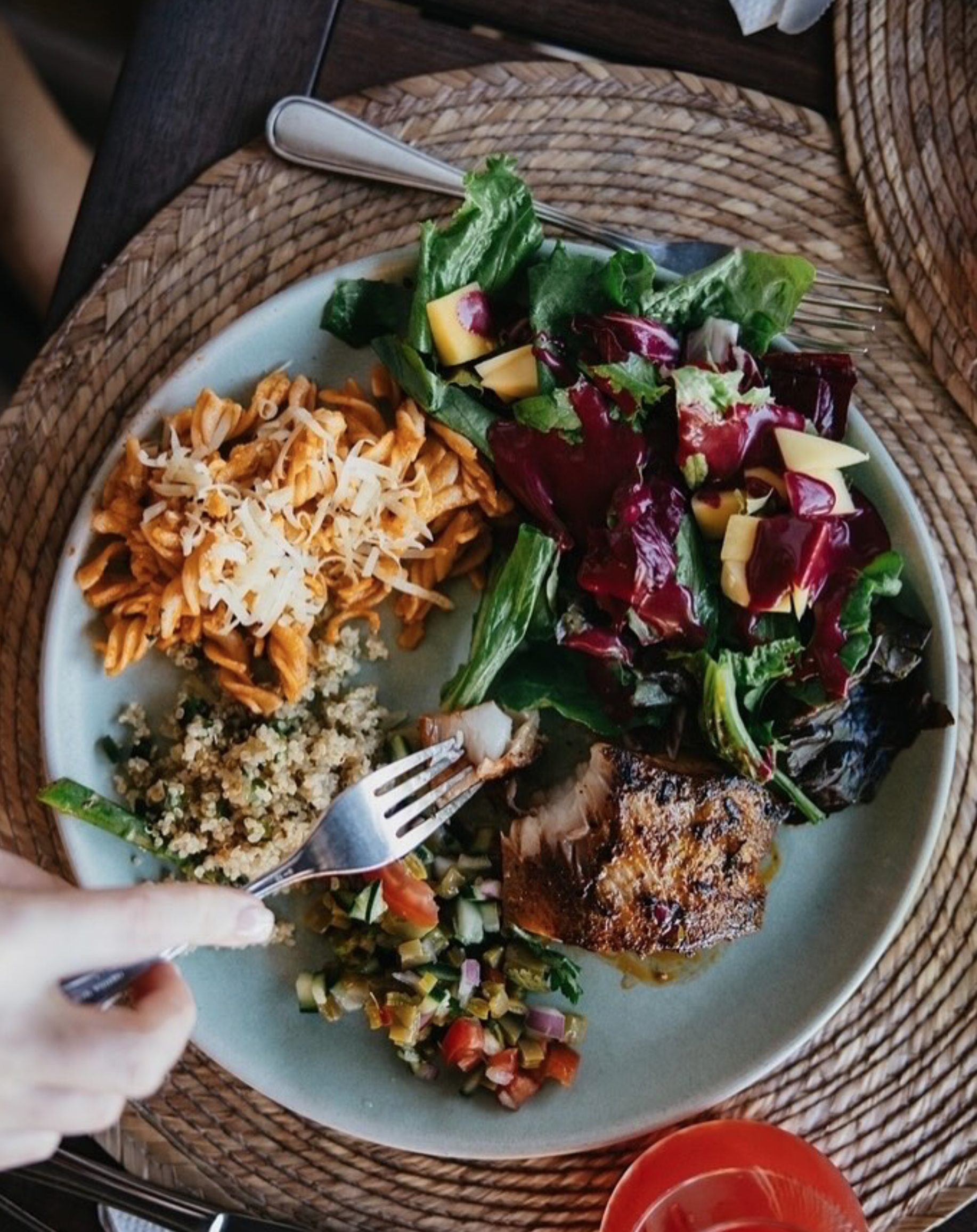 A plate with a variety of foods including pasta with cheese, quinoa, a salad with greens and cheese, grilled meat, and a vegetable mixture, with a fork and knife on the plate.