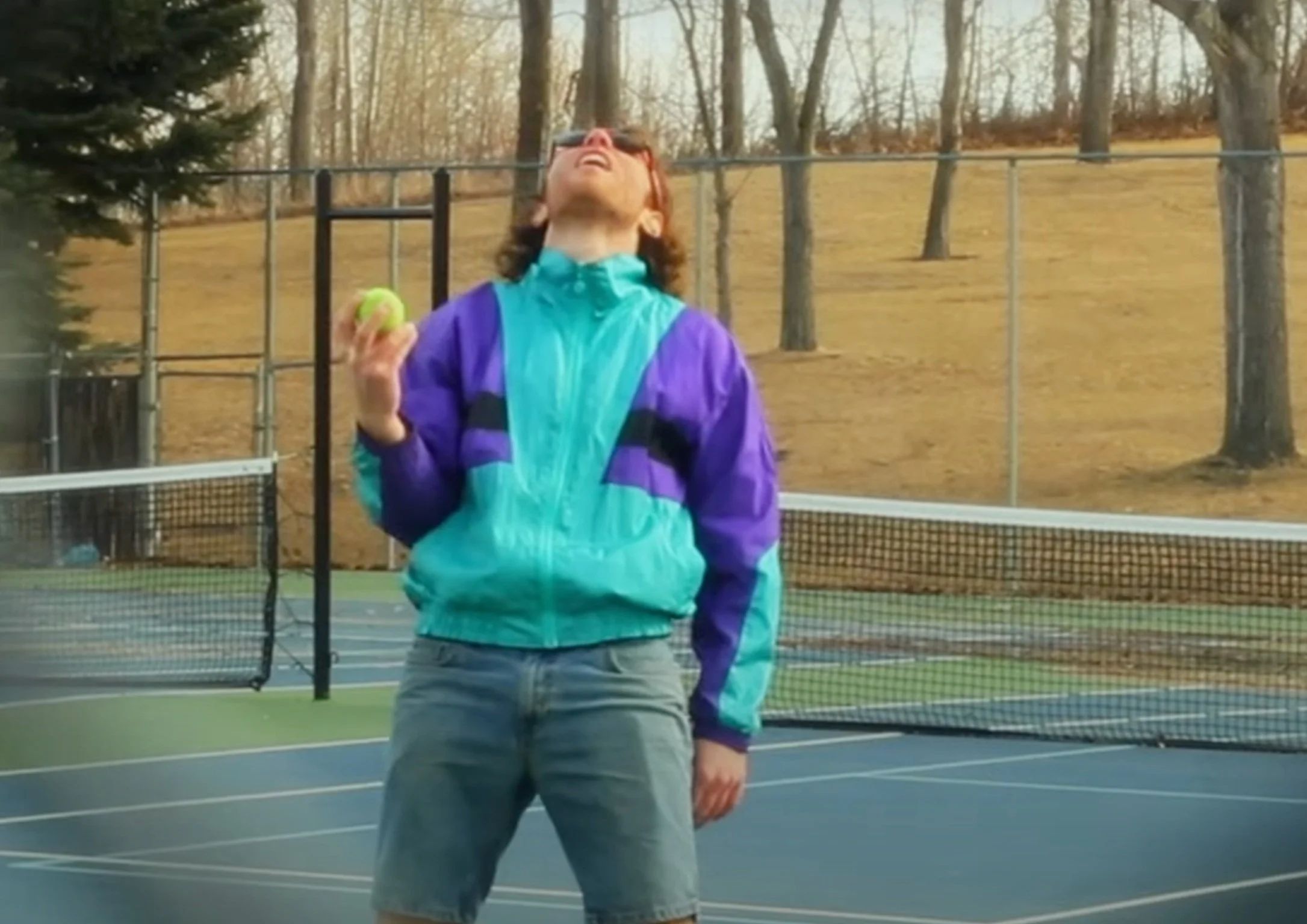 Person wearing a colorful windbreaker holding a tennis ball on a tennis court