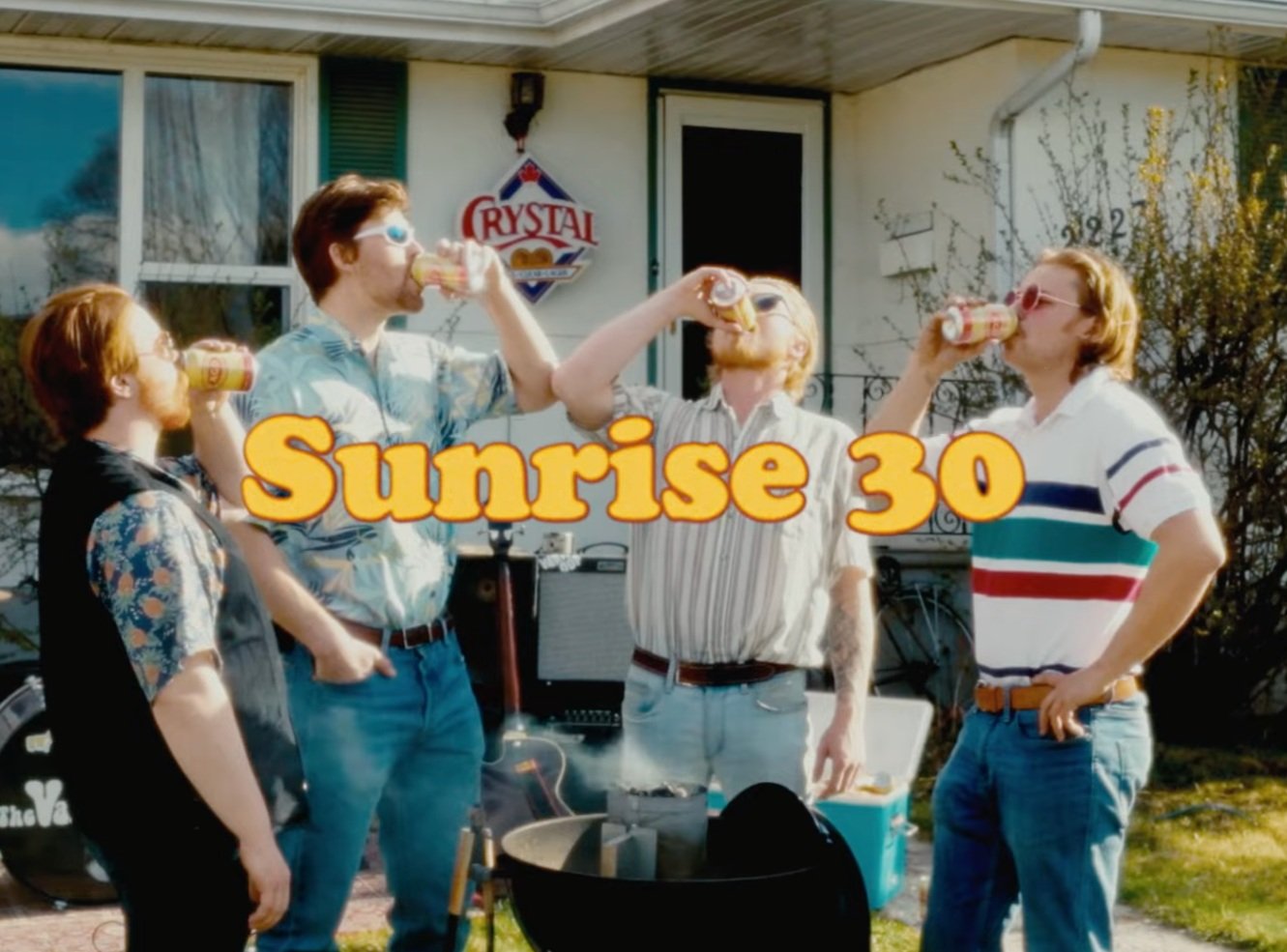 Four men wearing sunglasses are drinking cans of beer or soda outdoors in front of a house, with 'Sunrise 30' written across the image.