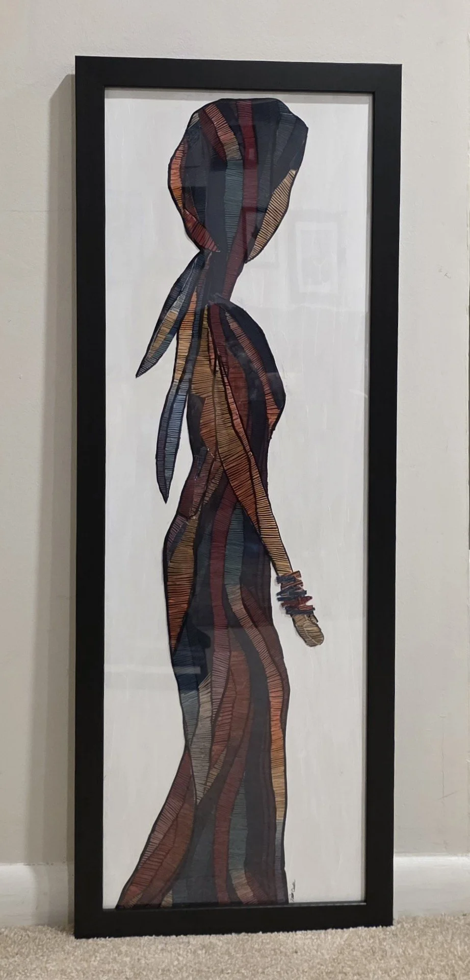 Colorful silhouette of a woman in profile made from fabric outlined with multicolored lines, framed and leaning against a white wall.