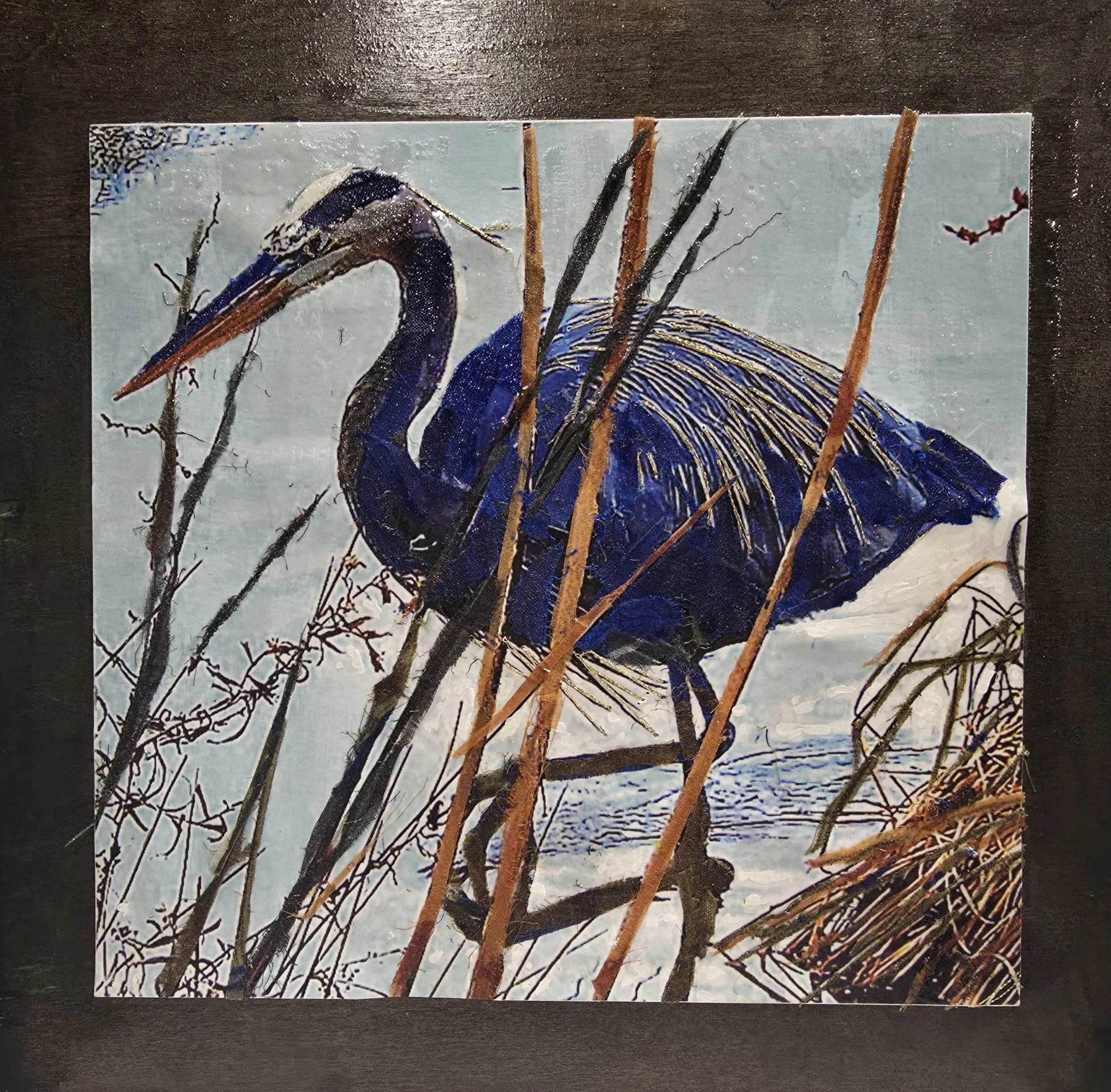 A giclee heron embellished with paint, fabric and thread mounted on a wooden board.
