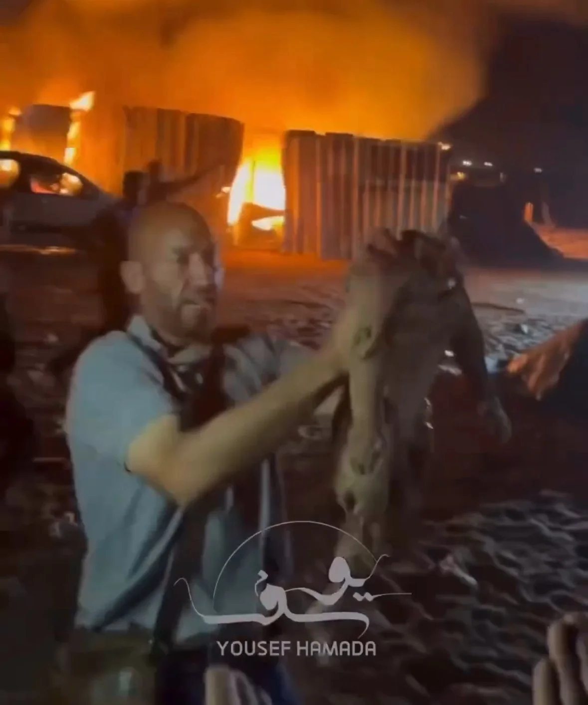   A man carries the beheaded body of an infant in Rafah after an Israeli airstrike in May 2024, as fires burn through the refugee camp behind him.  