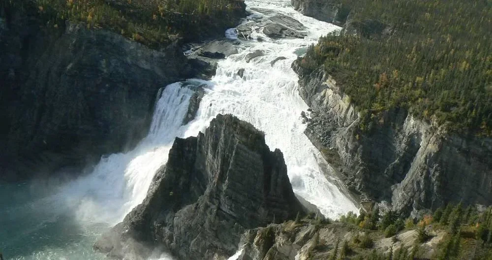 Waterfall flowing through a canyon with rocky walls and greenery on the cliff edges.